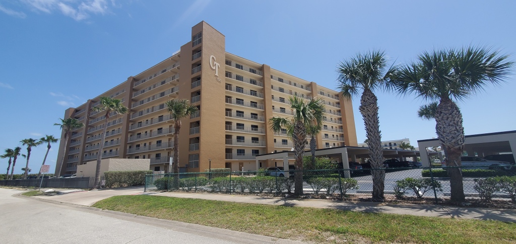 Cape Towers condominium in Cape Canaveral Florida. The photo shows the North West view of the condo that includes the parking lot and palm trees lining the street. 